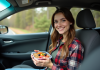 Conseils pour bien manger lors d’un road trip : aliments et astuces à connaître Jeune femme dans la voiture mangeant un fruit frais